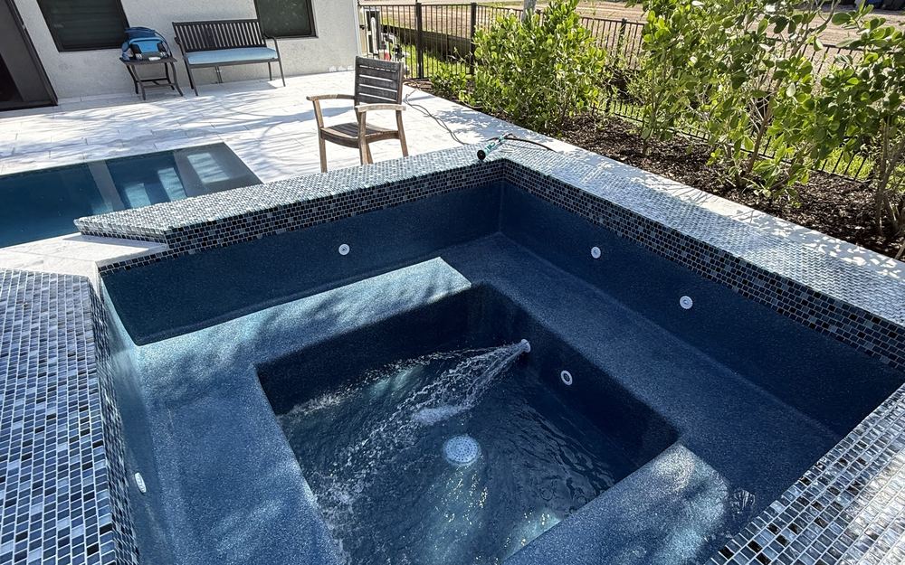 Raised spillover spa with glass mosaic tile flowing into a pool